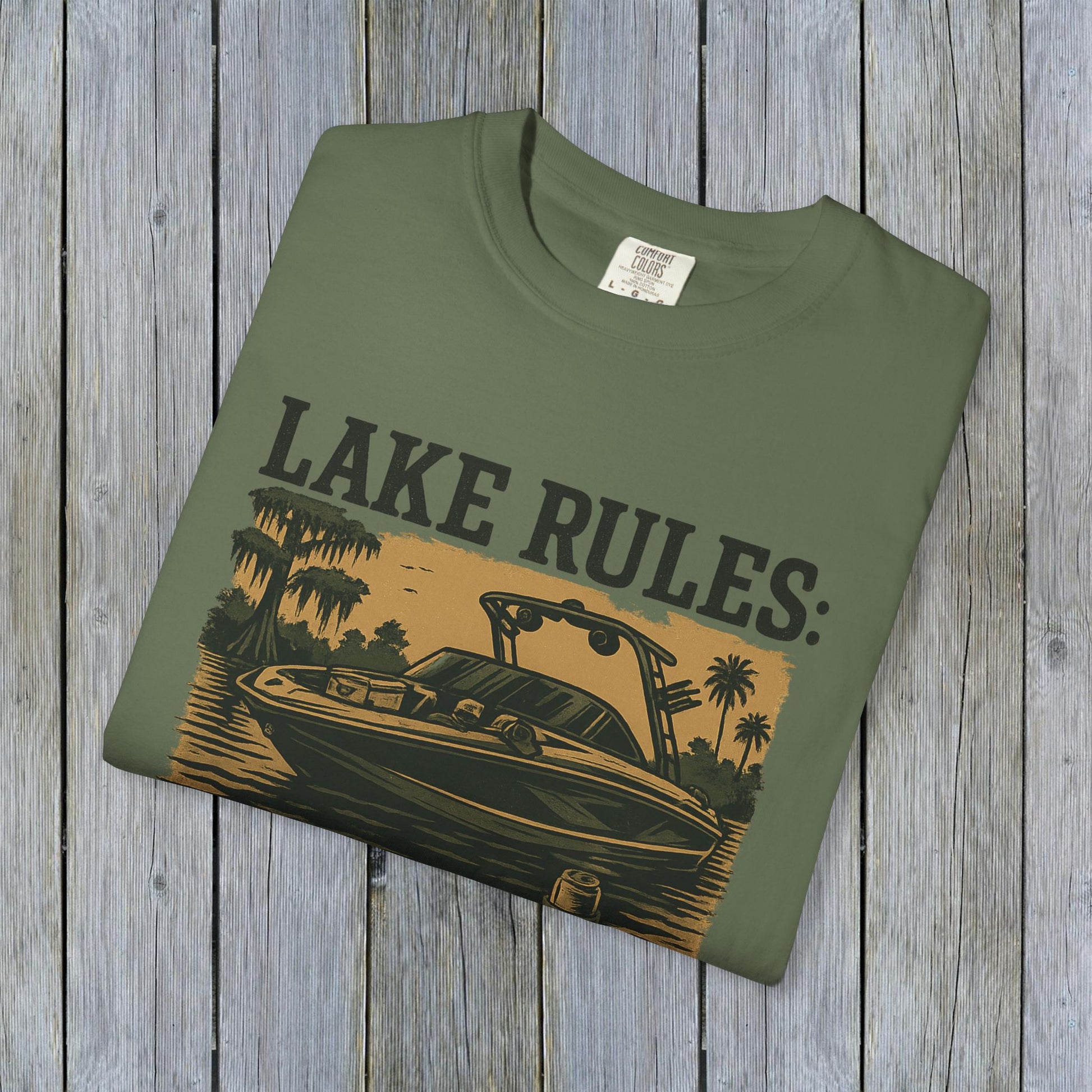 Unisex Garment-Dyed Lake Rules Tee displayed flat in olive green, featuring a vintage boat graphic with the text 'LAKE RULES:' in stylish print for an adventurous look.