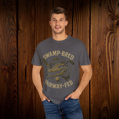 Model wearing the Unisex Swamp-Bred Fairway-Fed Tee in a neutral tone, standing against a rustic wooden backdrop. The tee features a stylish design ideal for golf enthusiasts, available in sizes S to 4XL.
