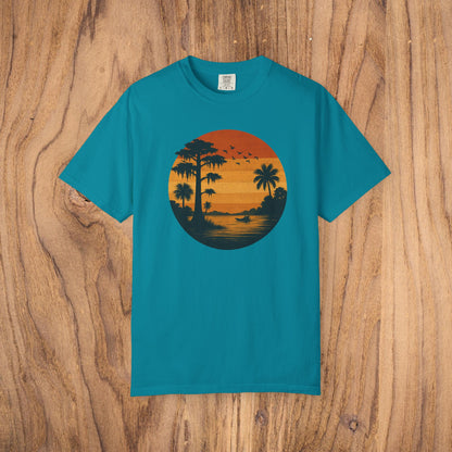 Unisex Garment-Dyed Sunset Tee in turquoise with a striking sunset illustration that includes palm trees and birds. Made from soft 100% cotton, available in sizes S to 4XL.
