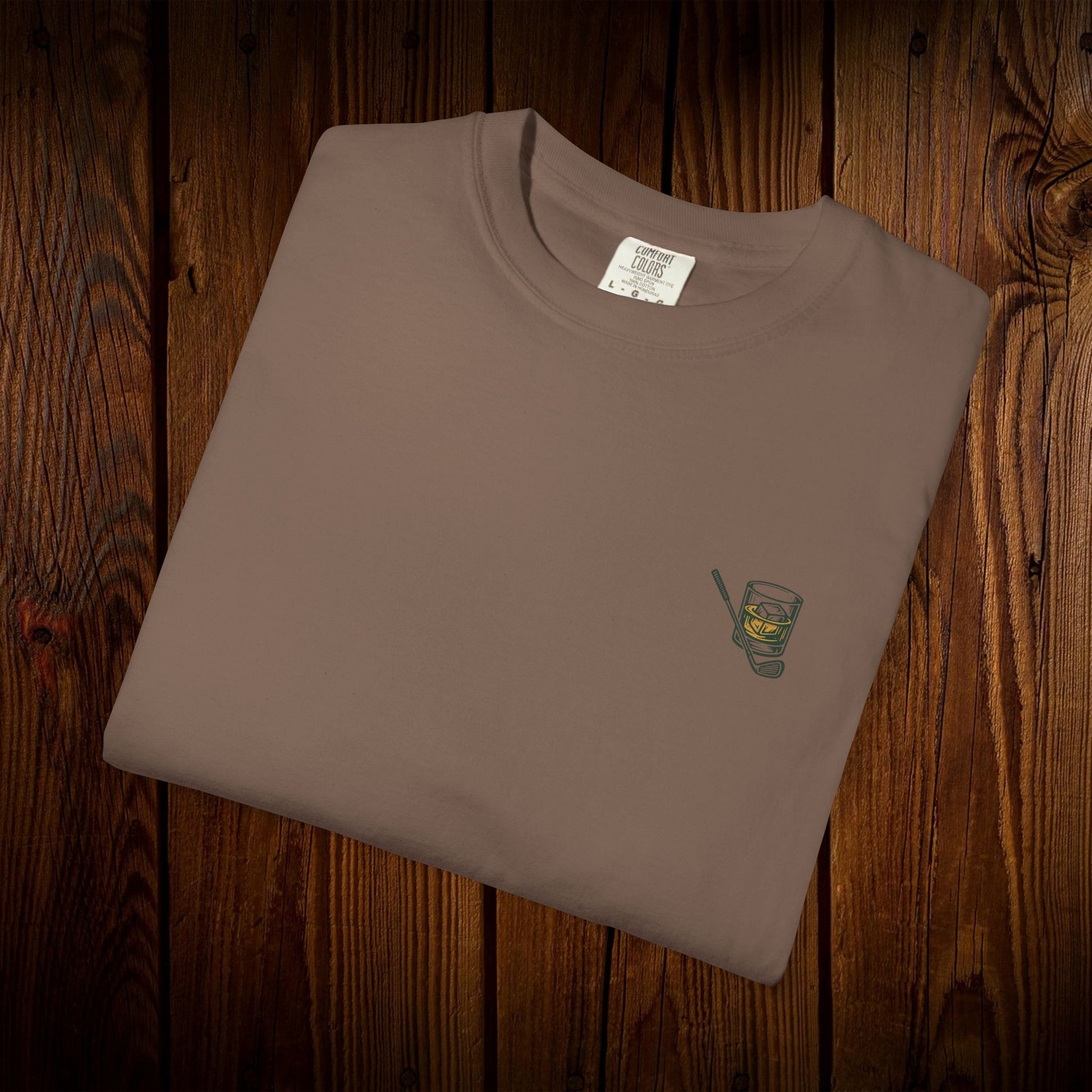 Men's Golf & Whiskey Tee neatly folded, displaying an intricate whiskey glass design on a natural tee, perfect for relaxed occasions and connecting with fellow whiskey lovers.
