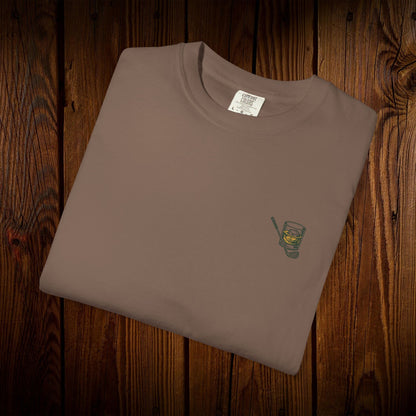 Men's Golf & Whiskey Tee neatly folded, displaying an intricate whiskey glass design on a natural tee, perfect for relaxed occasions and connecting with fellow whiskey lovers.