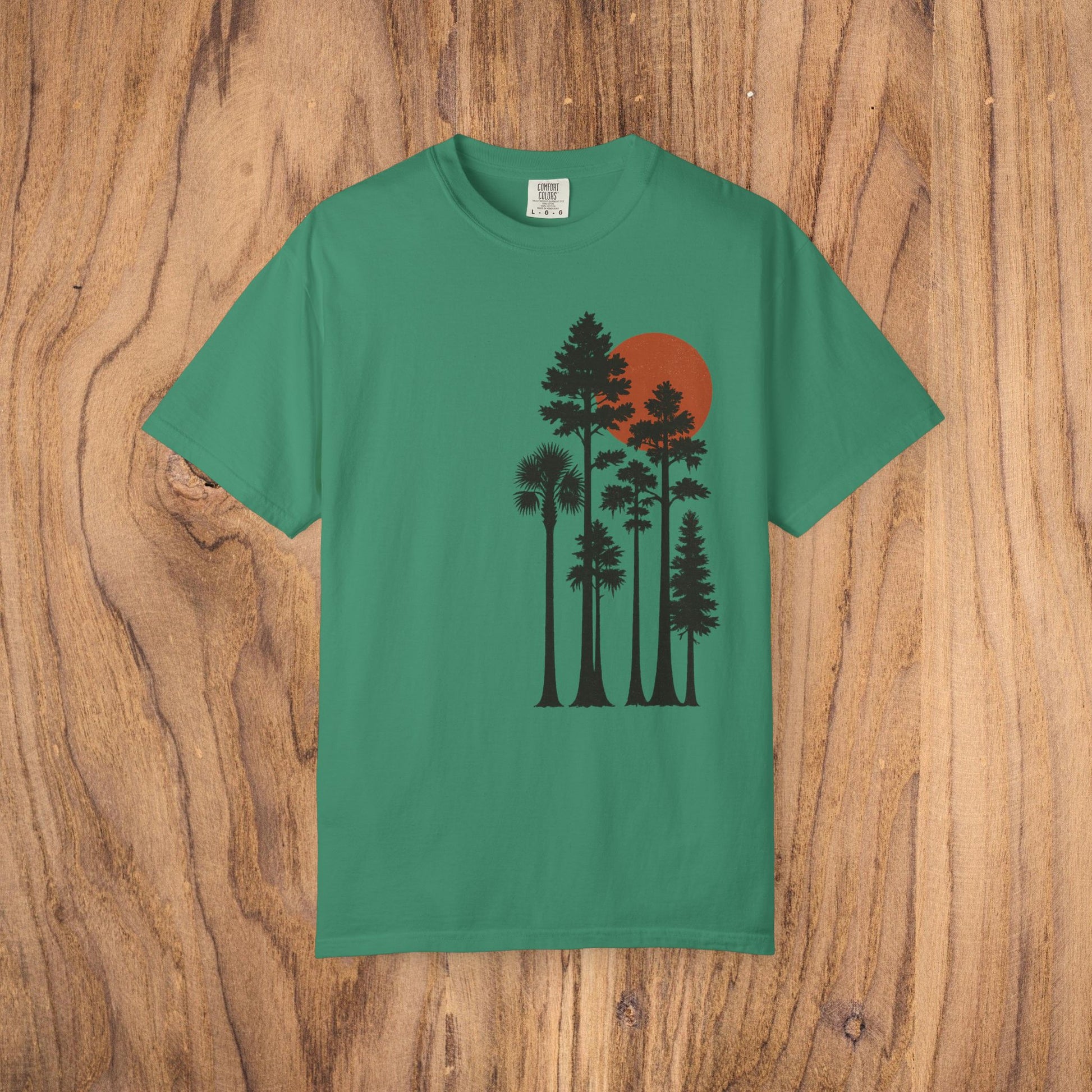 Sunset Trees Unisex T-Shirt in green, made of soft 100% cotton with a unique garment-dyed finish, featured against a wooden backdrop.