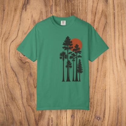 Sunset Trees Unisex T-Shirt in green, made of soft 100% cotton with a unique garment-dyed finish, featured against a wooden backdrop.