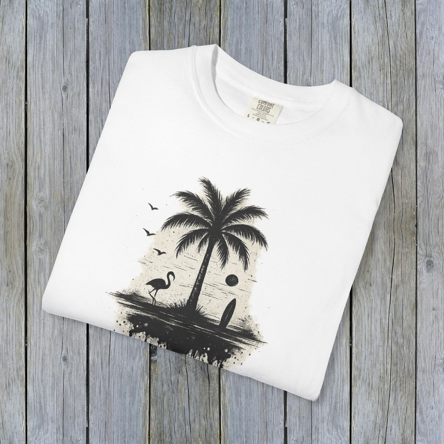 Tropical Sunset Graphic Tee displayed on a wooden background, showcasing a vibrant palm tree and flamingo design. Made from 100% cotton, available in sizes S-4XL for a comfortable fit.