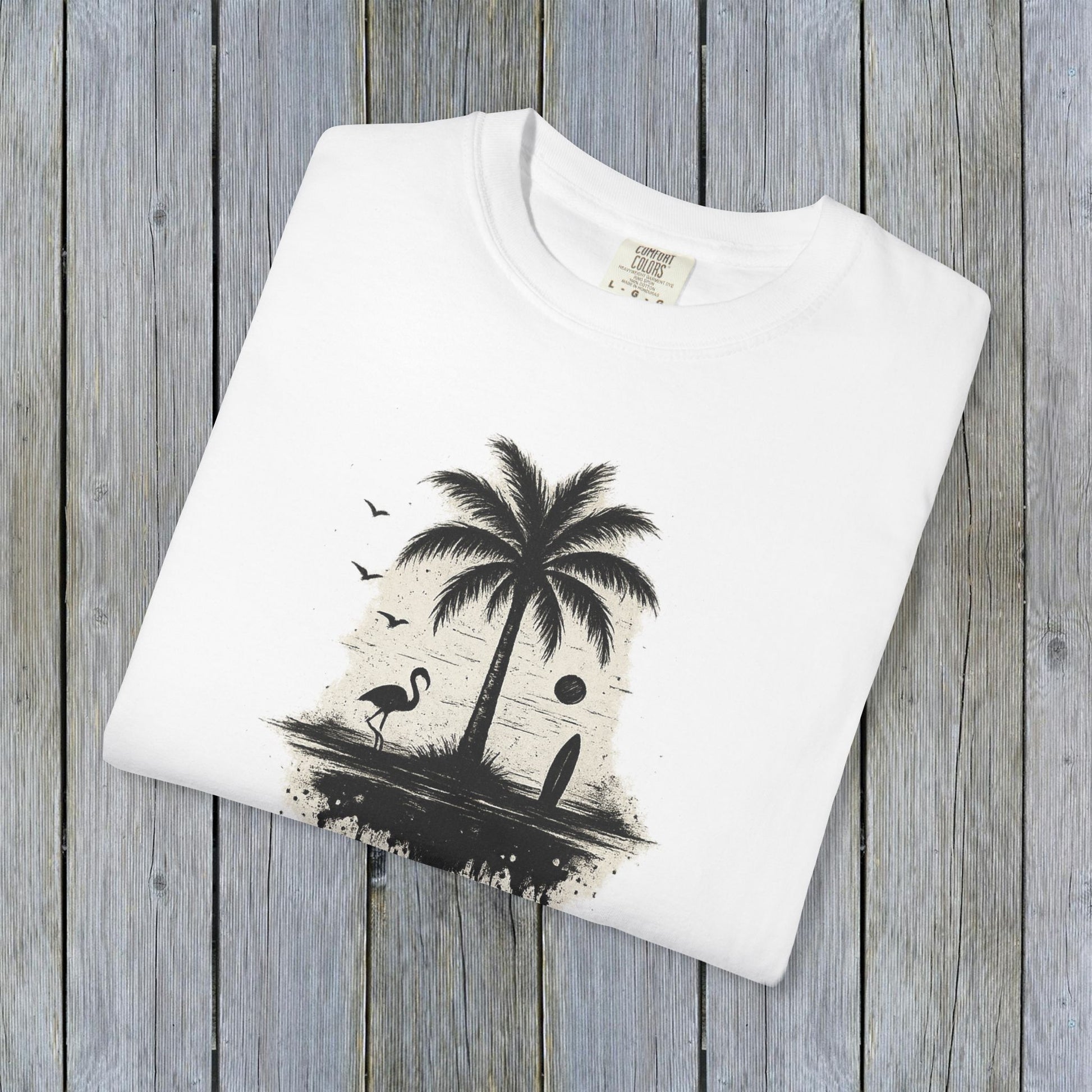 Tropical Sunset Graphic Tee displayed on a wooden background, showcasing a vibrant palm tree and flamingo design. Made from 100% cotton, available in sizes S-4XL for a comfortable fit.