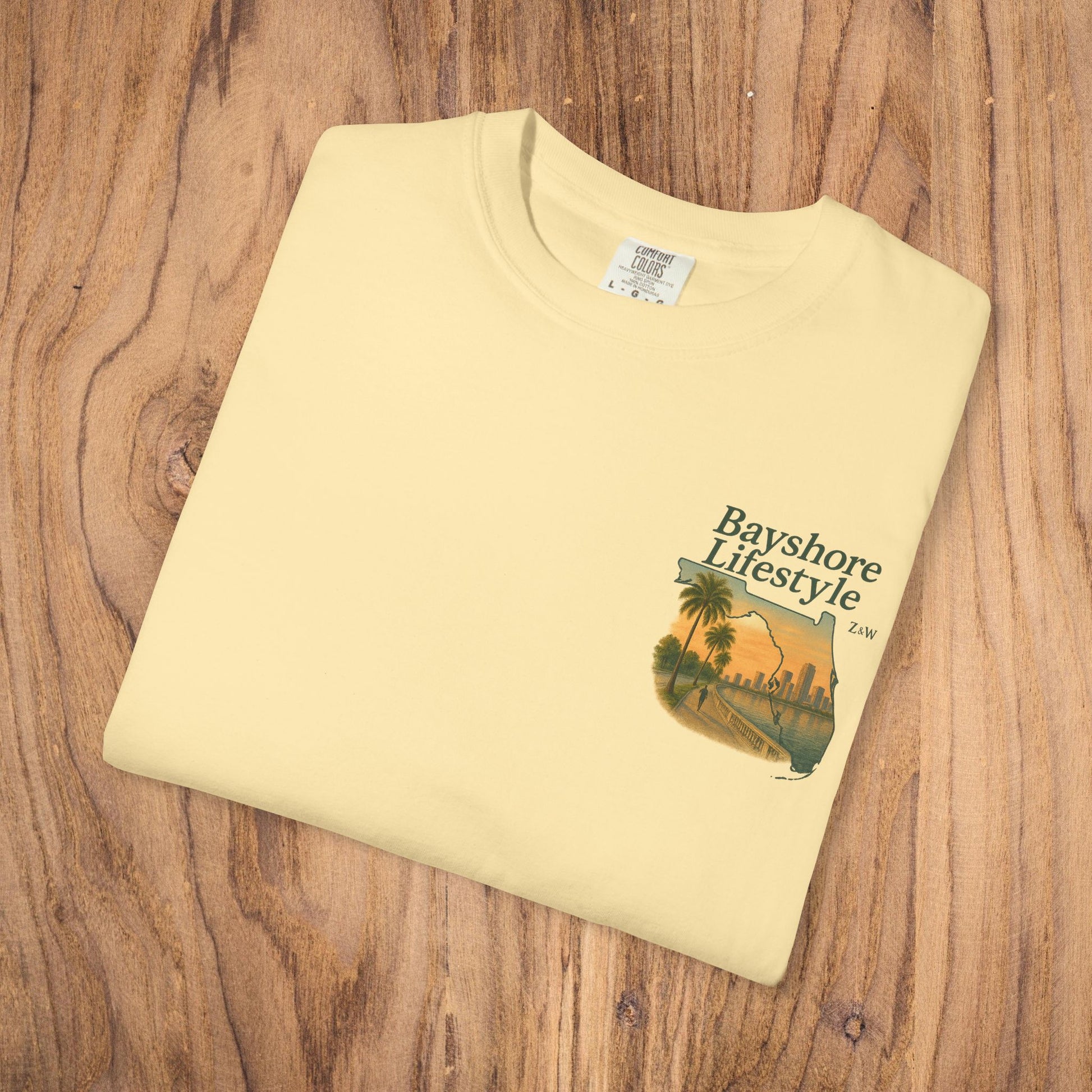 Bayshore Lifestyle Tee - Folded yellow t-shirt featuring a graphic design, laid out on a wooden surface.
