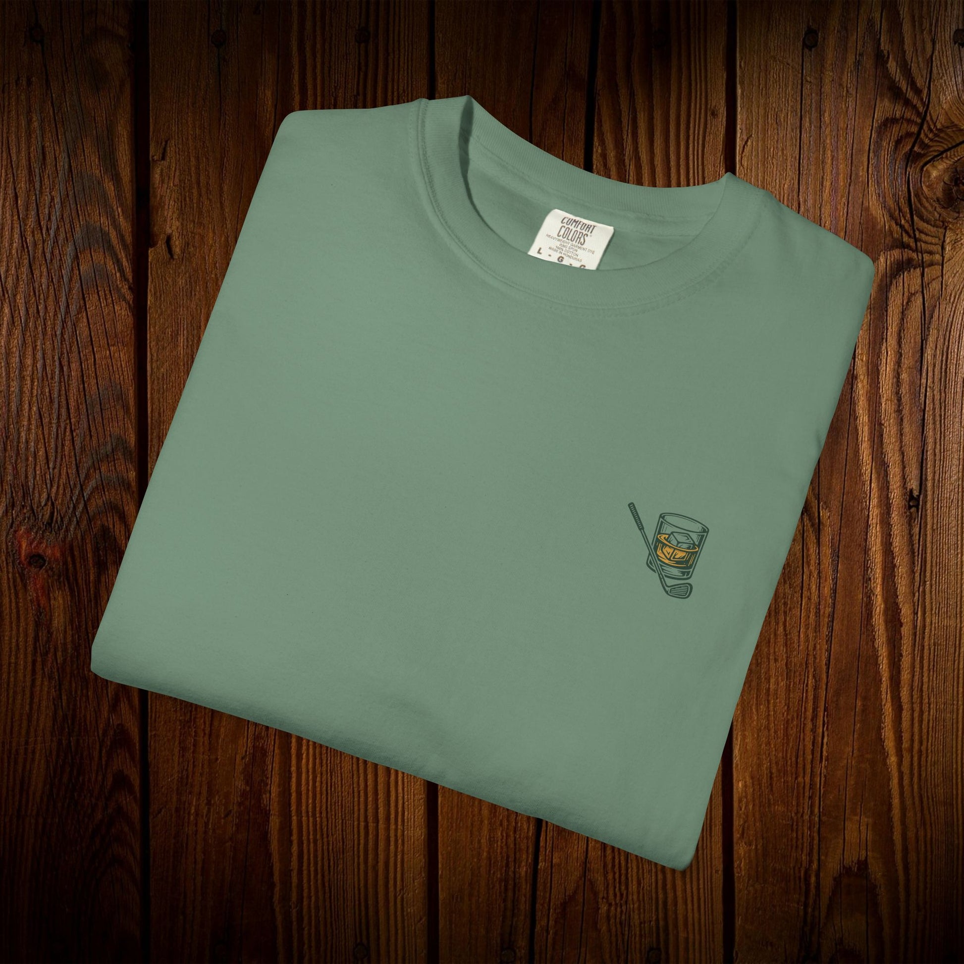 Folded Men's Golf & Whiskey Tee in natural color highlighting a classy whiskey glass illustration. Crafted from soft cotton, this shirt combines style and eco-friendliness.