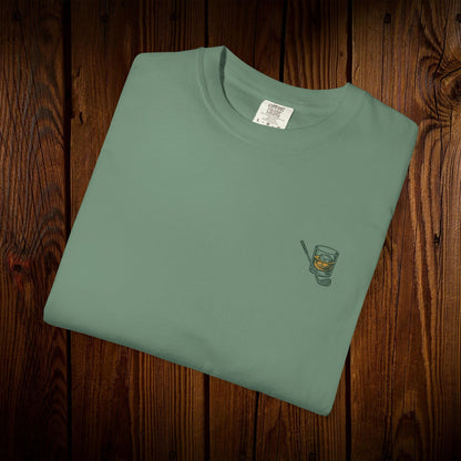 Folded Men's Golf & Whiskey Tee in natural color highlighting a classy whiskey glass illustration. Crafted from soft cotton, this shirt combines style and eco-friendliness.