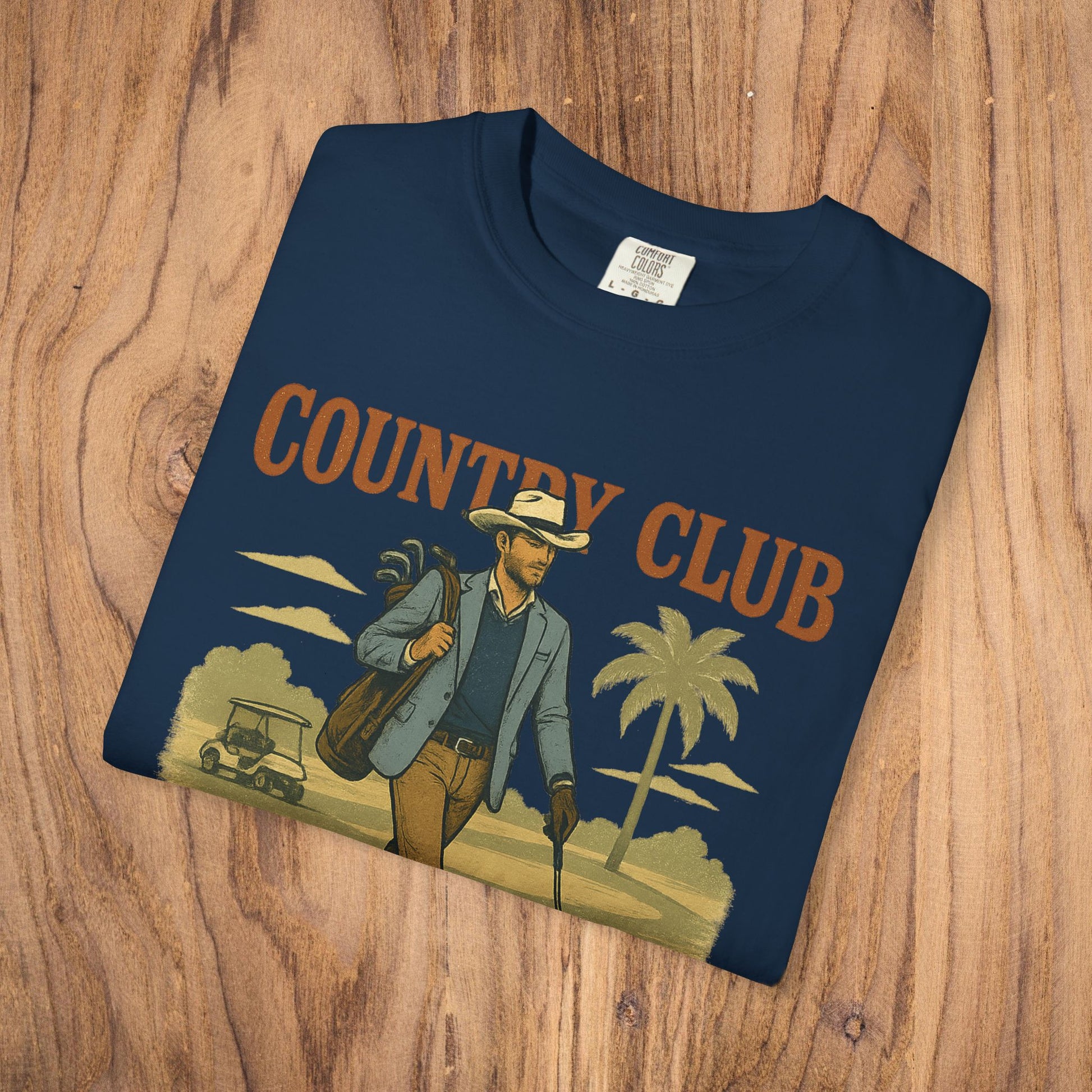 Country Club Cowboy Graphic Tee displayed on a wooden surface, showing a man dressed stylishly with golf equipment, perfect for casual wear.