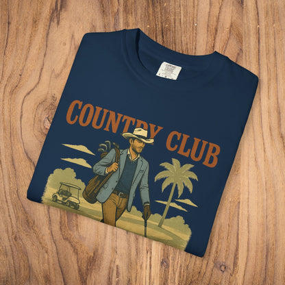 Country Club Cowboy Graphic Tee displayed on a wooden surface, showing a man dressed stylishly with golf equipment, perfect for casual wear.