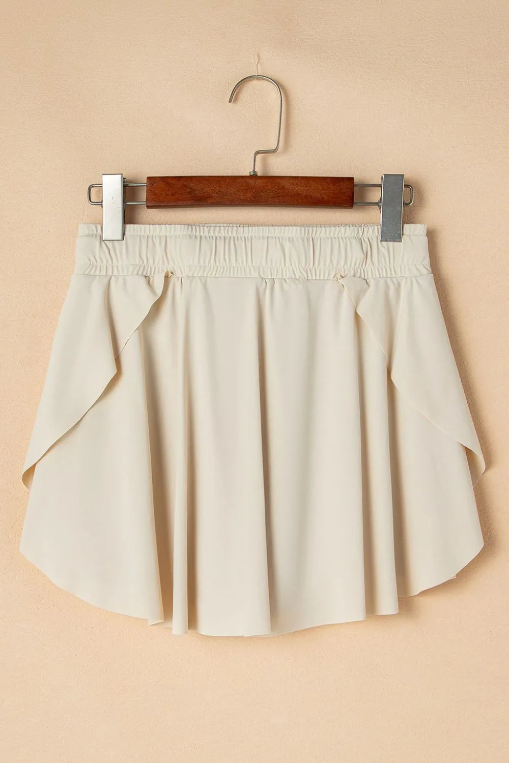 Drawstring High Waist Lined Active Skorts displayed on a hanger against a beige background, showcasing the flowy style and light color.