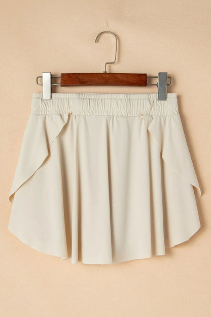 Drawstring High Waist Lined Active Skorts displayed on a hanger against a beige background, showcasing the flowy style and light color.