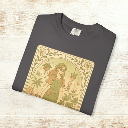 Rooted One Tarot Tee in charcoal gray, featuring a whimsical design with a girl surrounded by plants and butterflies, made from ethically sourced cotton, available in sizes S-4XL.