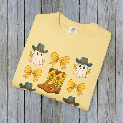 Cute Halloween T-Shirt design featuring cheerful ghosts, cowboy boots, and yellow bows, neatly folded and displayed against a weathered wooden surface, perfect for stylish eco-friendly attire.
