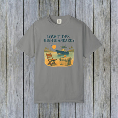 Garment-Dyed Low Tides High Standards T-Shirt in grey color, displaying an idyllic beach scene with a chair, cooler, and boat. This shirt is made from soft 100% US cotton and comes in sizes S-4XL.