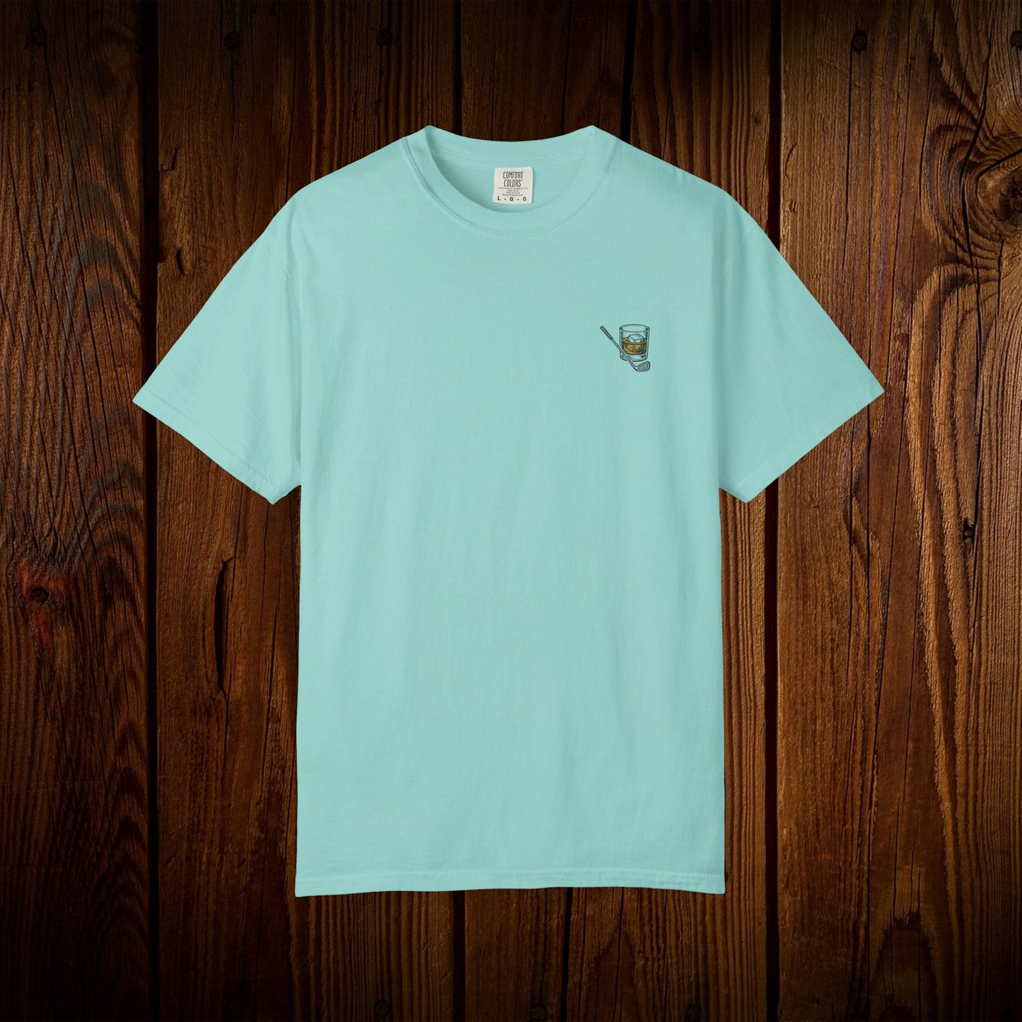 Men's Golf & Whiskey Tee in mint color, highlighting a small logo on the front, presented against a warm wood texture for an eco-friendly appeal.