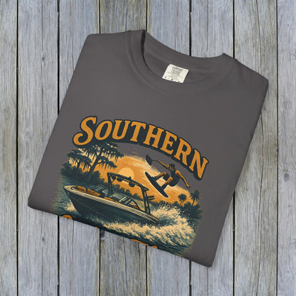 Southern Lake Flow T-Shirt laid flat on a wooden backdrop, in grey color with a graphic of a boat and wakeboarder, emphasizing durability and sustainable materials from 100% US cotton.