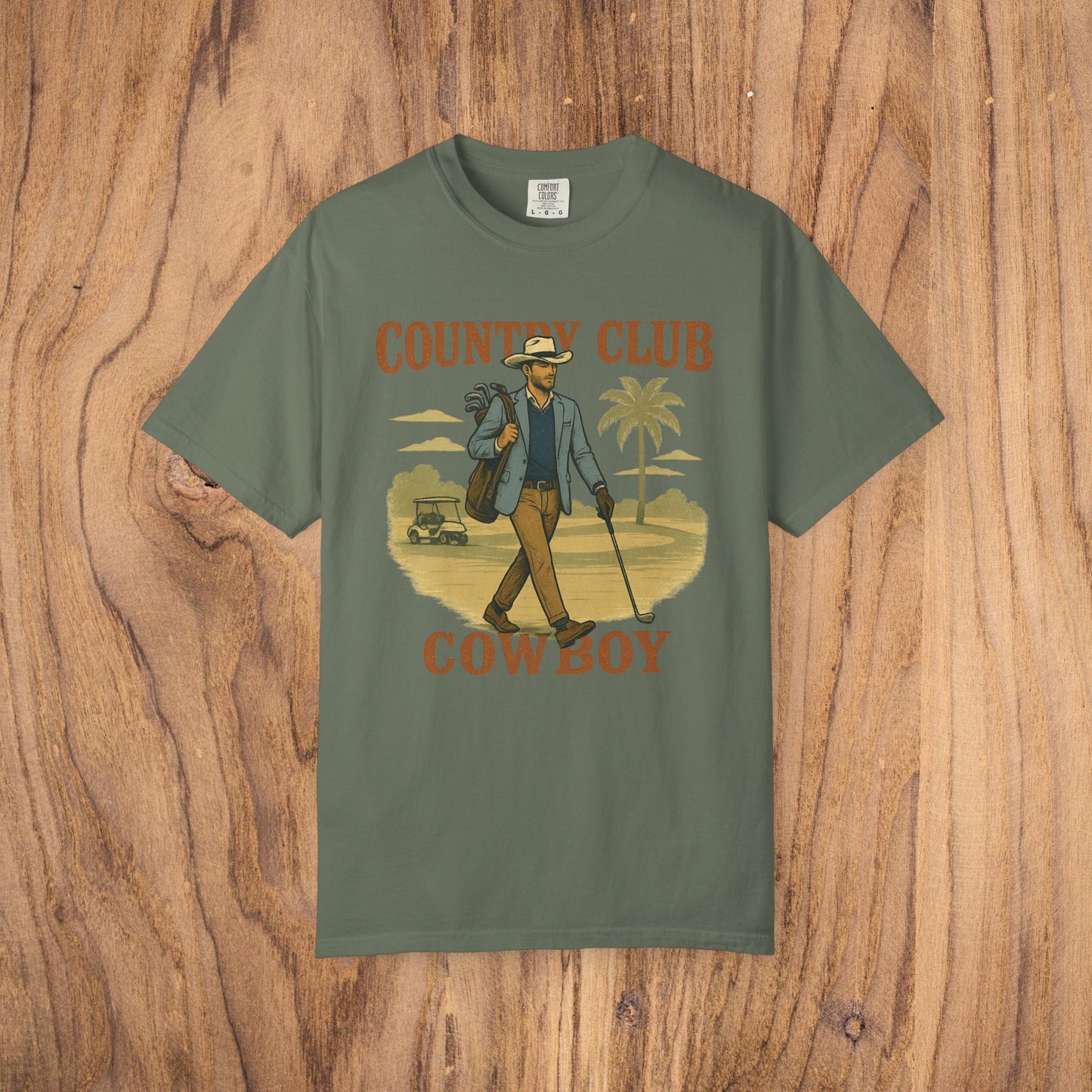 Country Club Cowboy Graphic Tee in olive green showcasing a cowboy strolling with a golf bag against a palm tree background, made of durable cotton fabric, with a comfortable ribbed collar and eco-friendly crewneck.