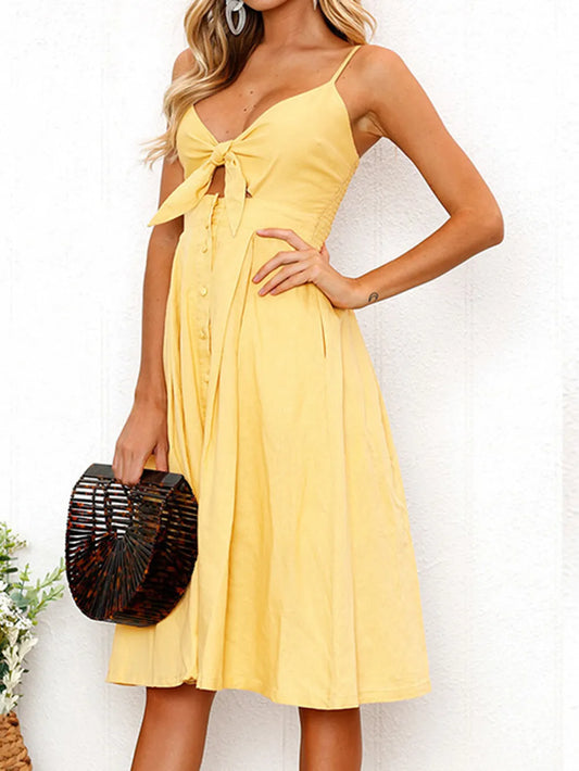 Side view of the Cutout Smocked Sweetheart Neck Cami Dress with Decorative Button and Opaque Design, highlighting the tied waist and flowy skirt worn by a model.