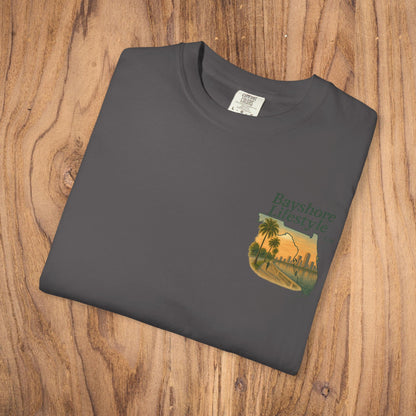 Bayshore Lifestyle Tee featuring a vibrant graphic, displayed on a wooden surface, highlighting its 100% cotton lightweight fabric and ribbed neck design.