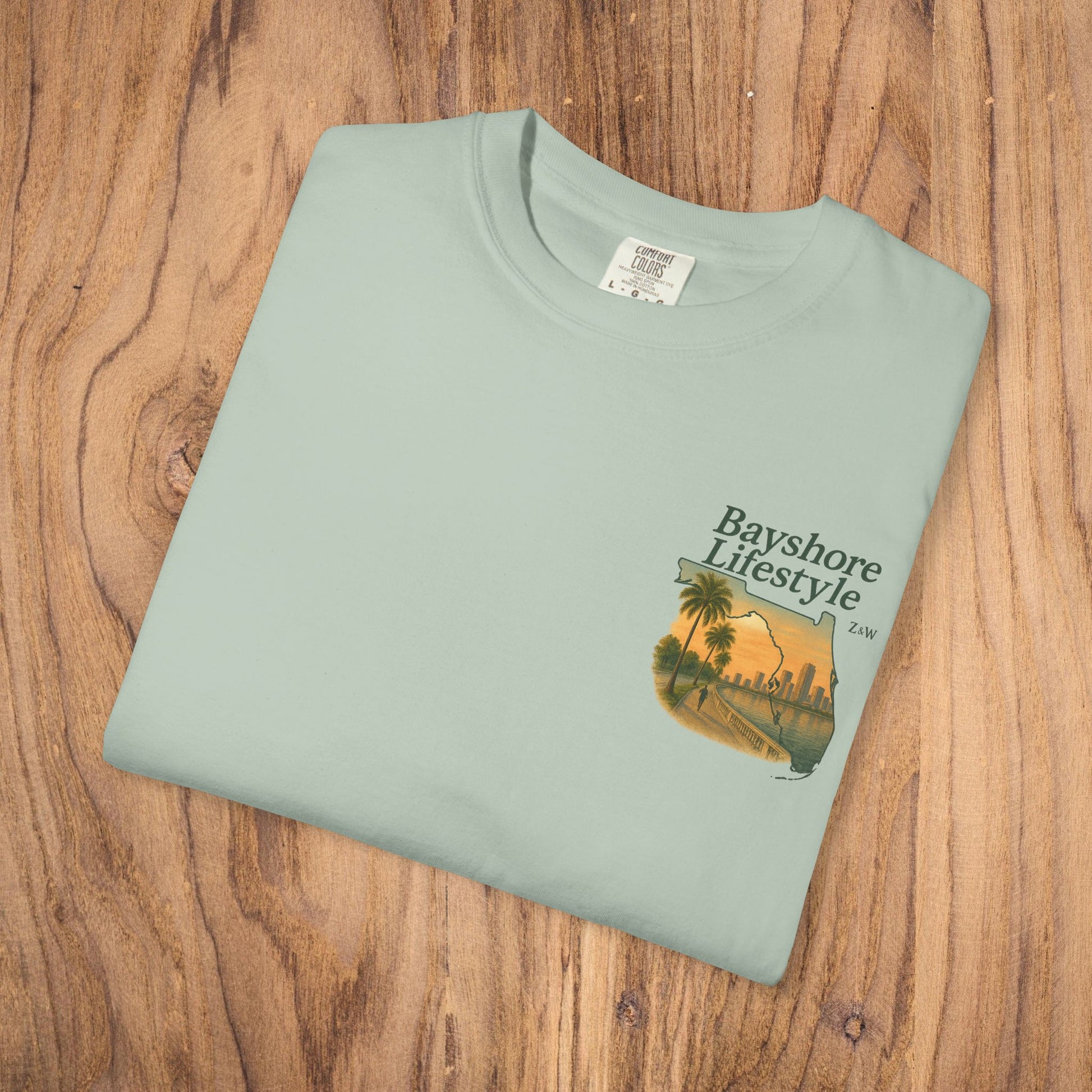 Bayshore Lifestyle Tee displayed flat on wood in mint green, emphasizing the softness of 100% cotton fabric.