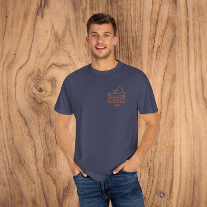 Unisex Florida Graphic Tee, featuring a stylish design, garment-dyed for a soft feel, perfect for casual wear. Model showcasing the shirt in a relaxed fit against a wooden backdrop, highlighting its versatile appeal and comfortable fit for all occasions.