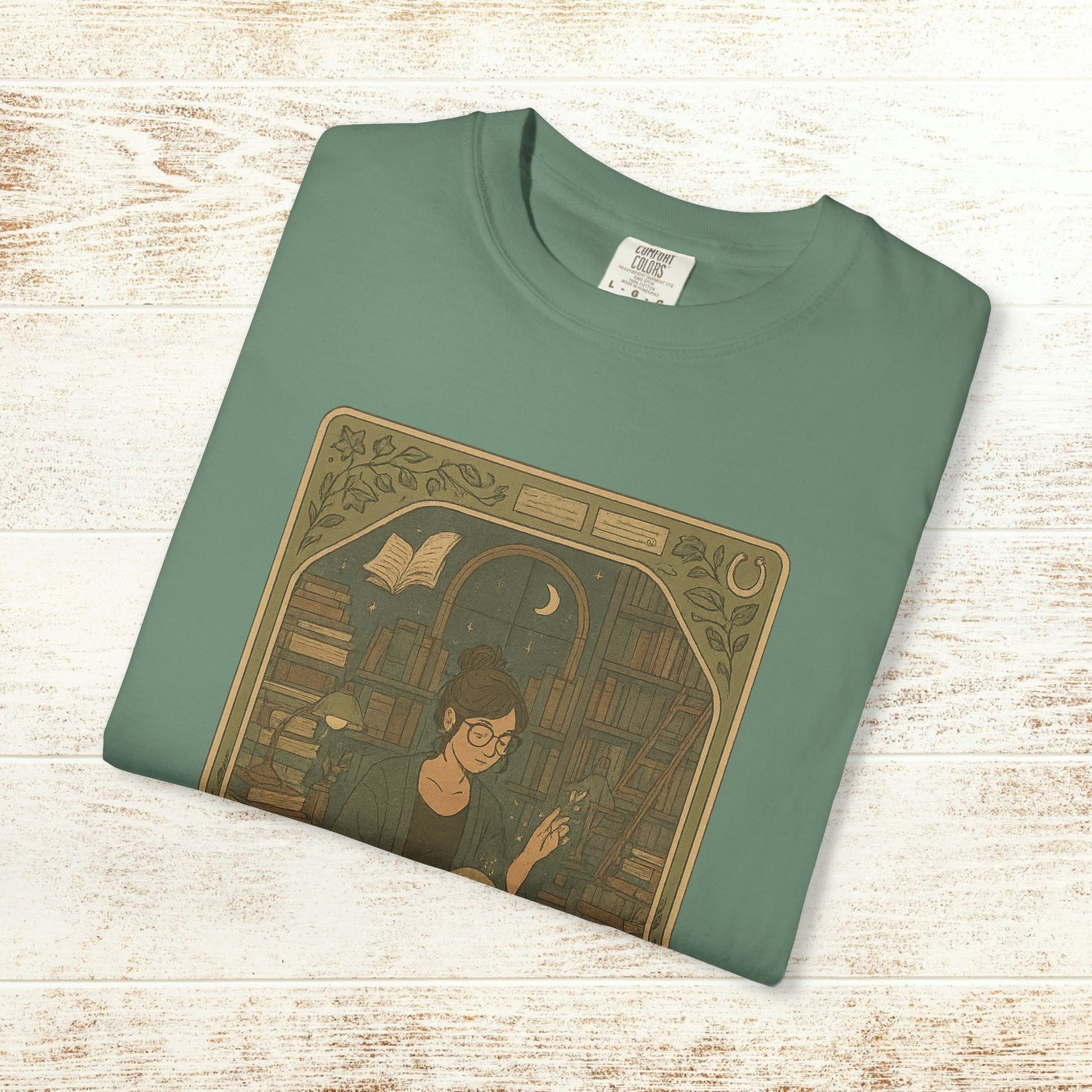 Page Turner Tarot Tee in teal, featuring a whimsical design of a woman reading surrounded by books, made from soft and eco-friendly cotton.