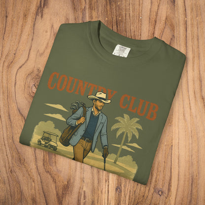 Country Club Cowboy Graphic Tee in an olive green color, displayed on a wooden backdrop, featuring a unique cowboy graphic design.
