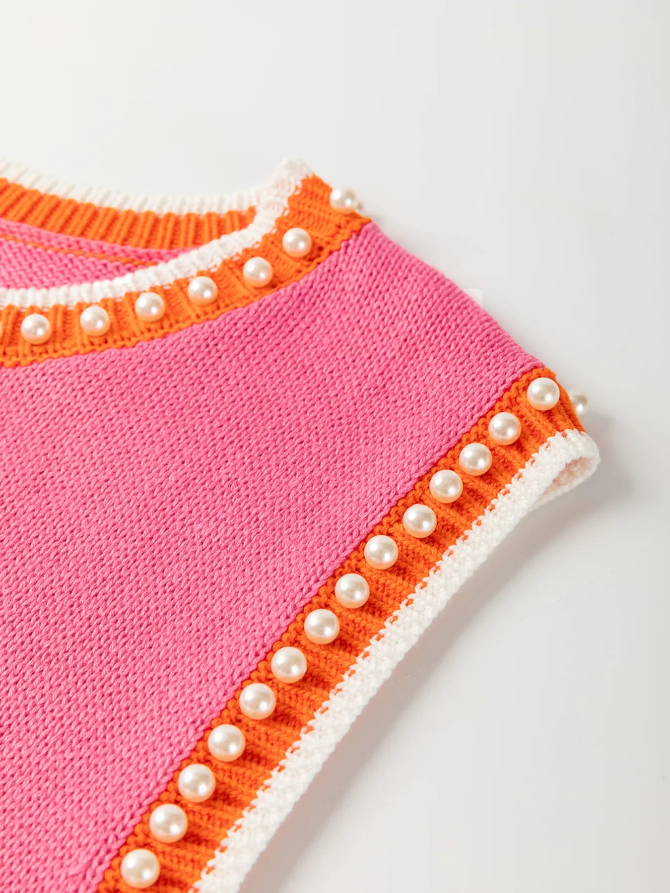 Close-up view of the Stylish Contrast Trim Pearl Detail Sweater Tank Top showcasing its unique pink texture and decorative pearl accents along the armholes.