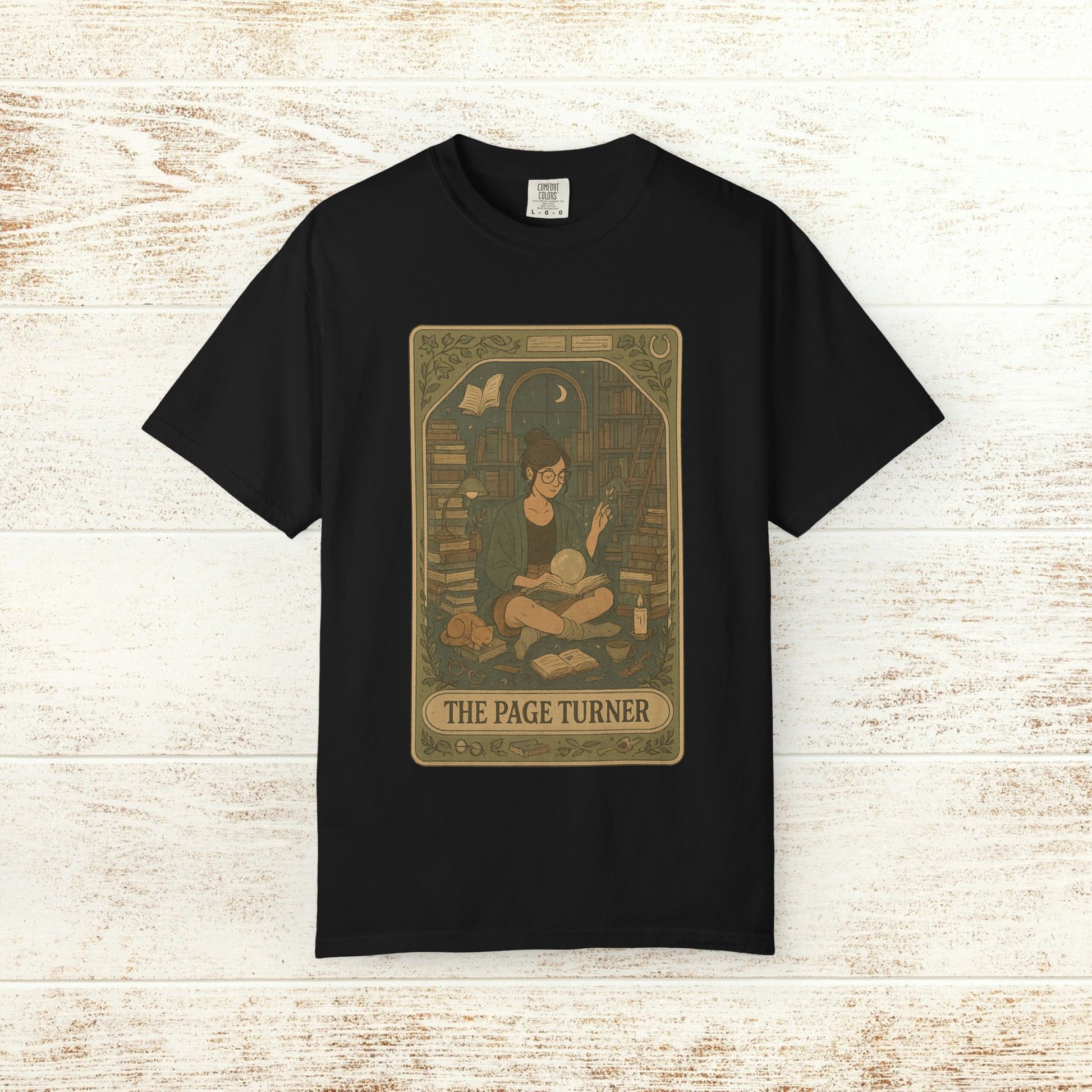 Page Turner Tarot Tee in black, presenting a creative illustration of a book enthusiast in a library, made from comfortable, ethically produced cotton, available in sizes S to 4XL.