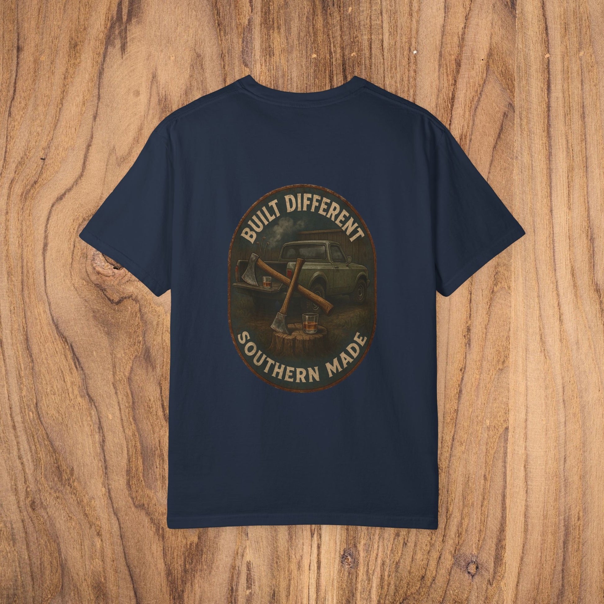 Back view of a Premium Southern Made T-Shirt in navy featuring the phrase 'BUILT DIFFERENT SOUTHERN MADE' over a vintage car graphic, set on a wooden background.