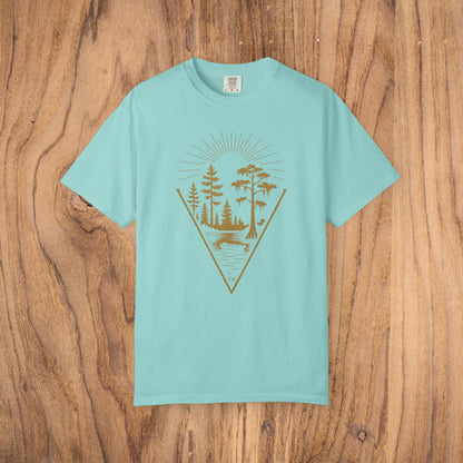 Nature Outdoor Vibes Tee displayed on a wooden background, showing the unique graphic design of trees and a lake in gold on a light teal shirt, crafted for comfort from 100% US cotton.
