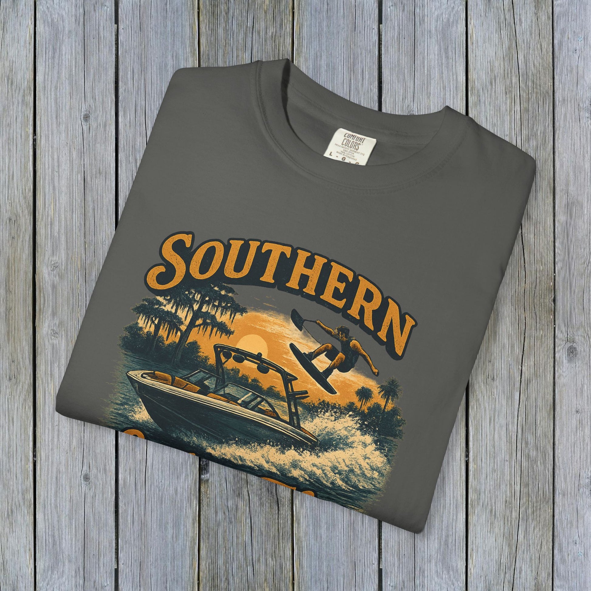 Southern Lake Flow T-Shirt displayed flat on a rustic wooden background in charcoal gray, featuring a water sports graphic, crafted sustainably with 100% US cotton.