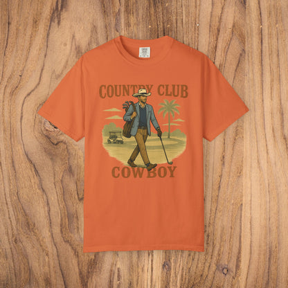 Country Club Cowboy Graphic Tee in vibrant orange, highlighting a cowboy with golf clubs in a casual design. Constructed from durable cotton fabric, perfect for outdoor activities.