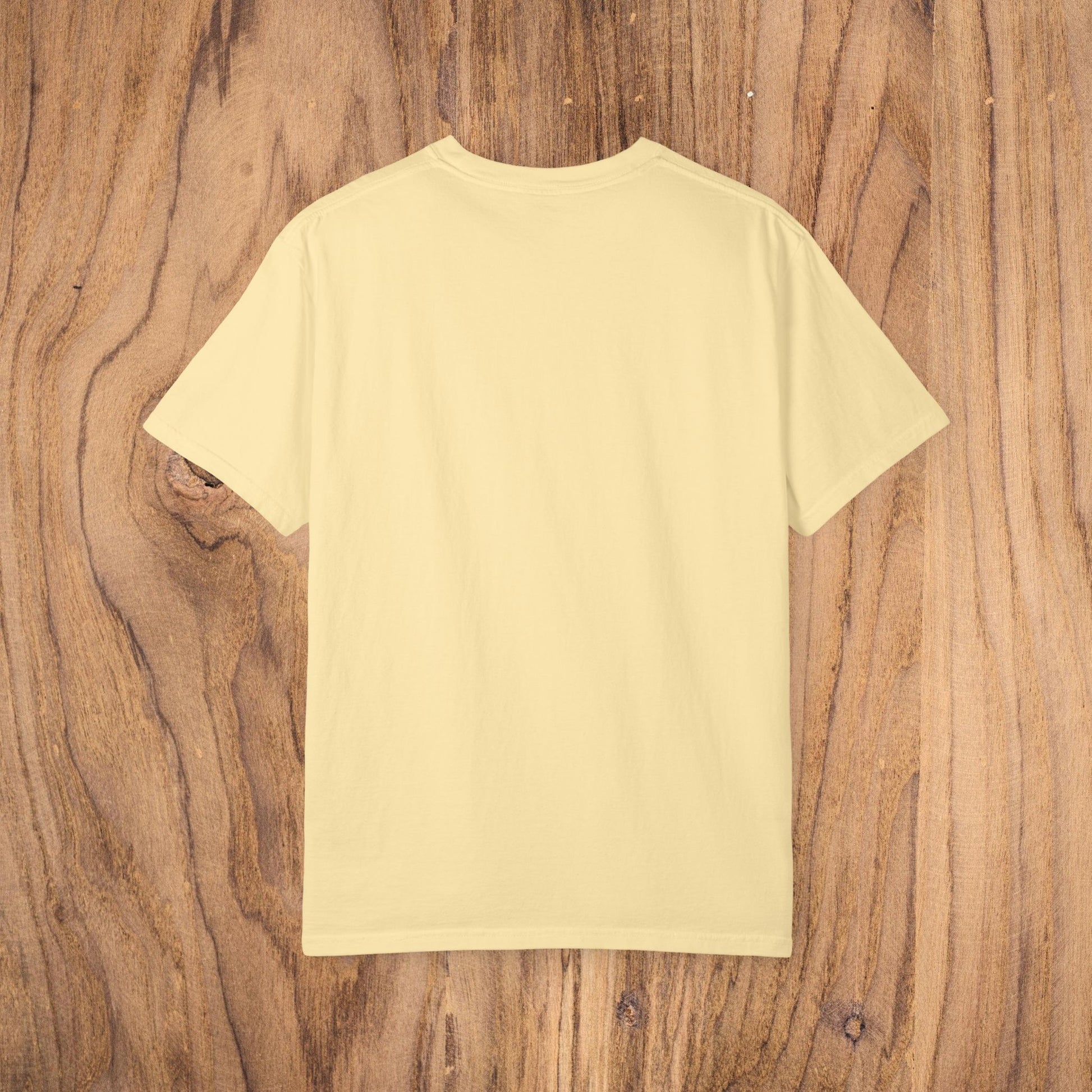 Back view of Unisex Sunset Palm Tree T-Shirt - Vibrant Garment-Dyed Cotton Tee for Men & Women showcasing a soft yellow fabric against a wooden surface.