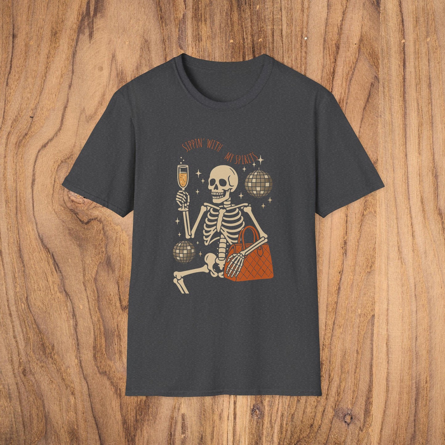 Spooky Spirits Graphic Tee displayed on a wooden surface, designed with a fun skeleton holding a drink and handbag, emphasizing the Halloween theme. Made with 100% cotton and Oeko-Tex certified for quality.