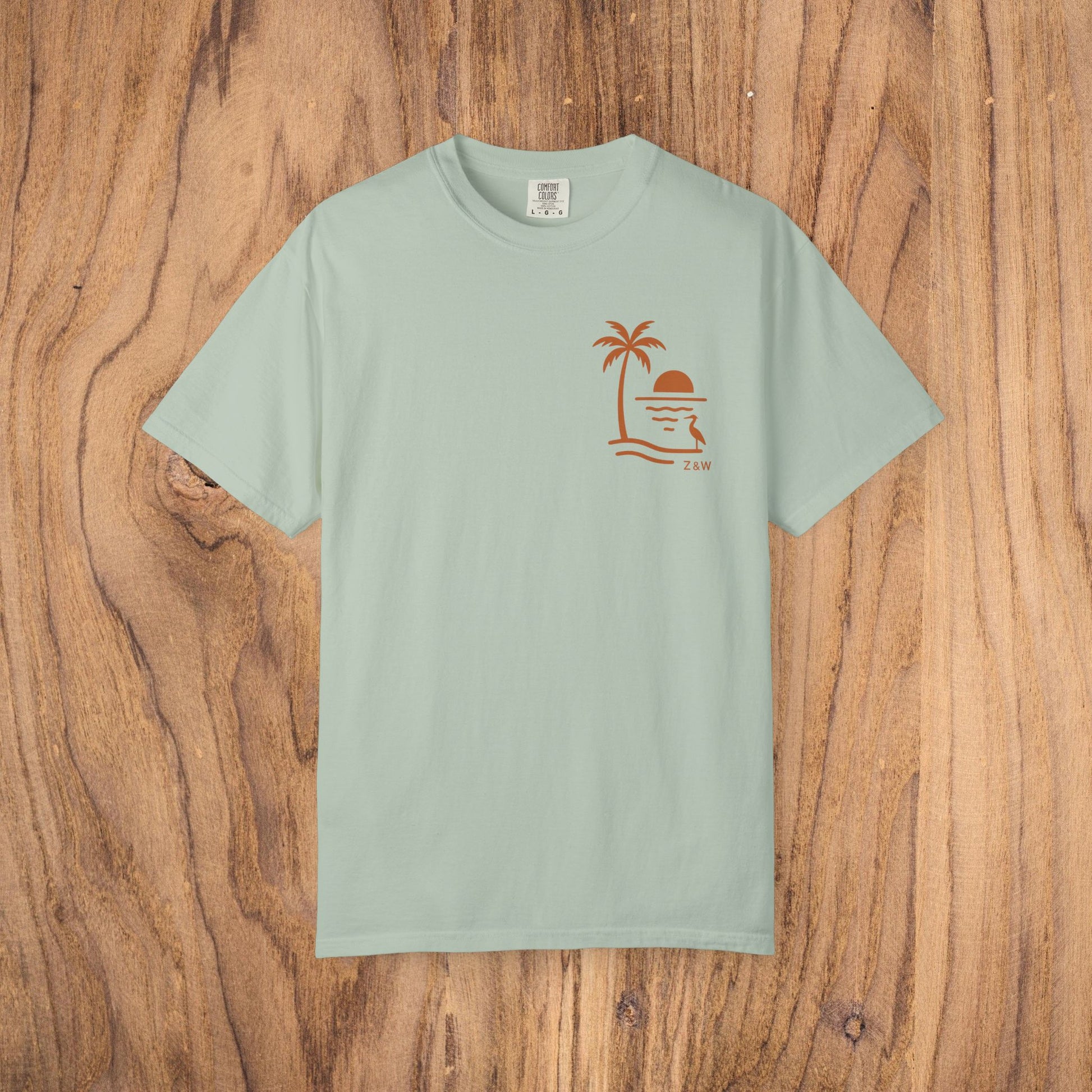 Unisex Sunset Palm Tree T-Shirt in soothing mint green. This vibrant garment-dyed cotton tee is perfect for both men and women, featuring a palm tree and sunset design. Choose from 58 colors.
