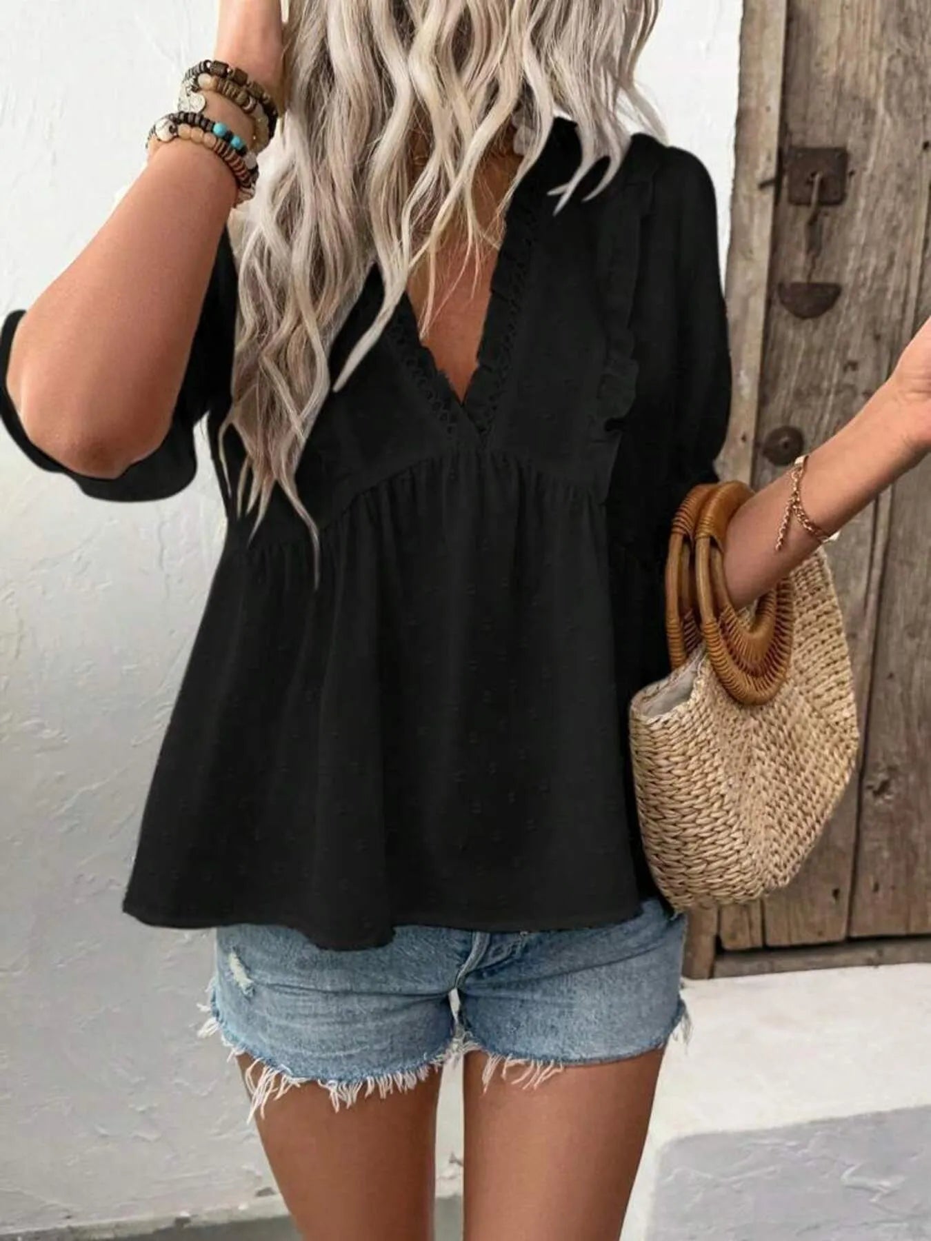 Styled shot of the black Swiss Dot Ruffled V-Neck Blouse, paired with denim shorts and a straw bag, embodying a trendy summer look.