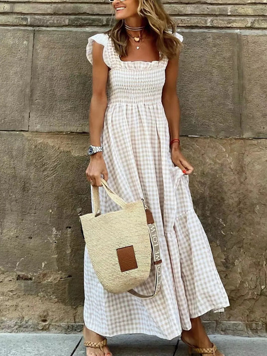 Stylish woman wearing a Gingham Maxi Dress with Ruffle Straps, Smocked Bodice & Tiered Design by Trendsi, holding a woven handbag against a stone wall.