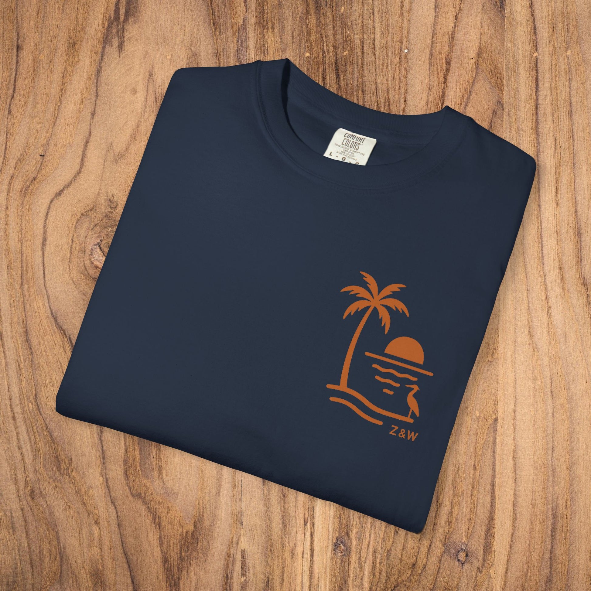 Close-up of a folded Unisex Sunset Palm Tree T-Shirt - Vibrant Garment-Dyed Cotton Tee for Men & Women in navy blue featuring a stylish palm tree and sunset design.