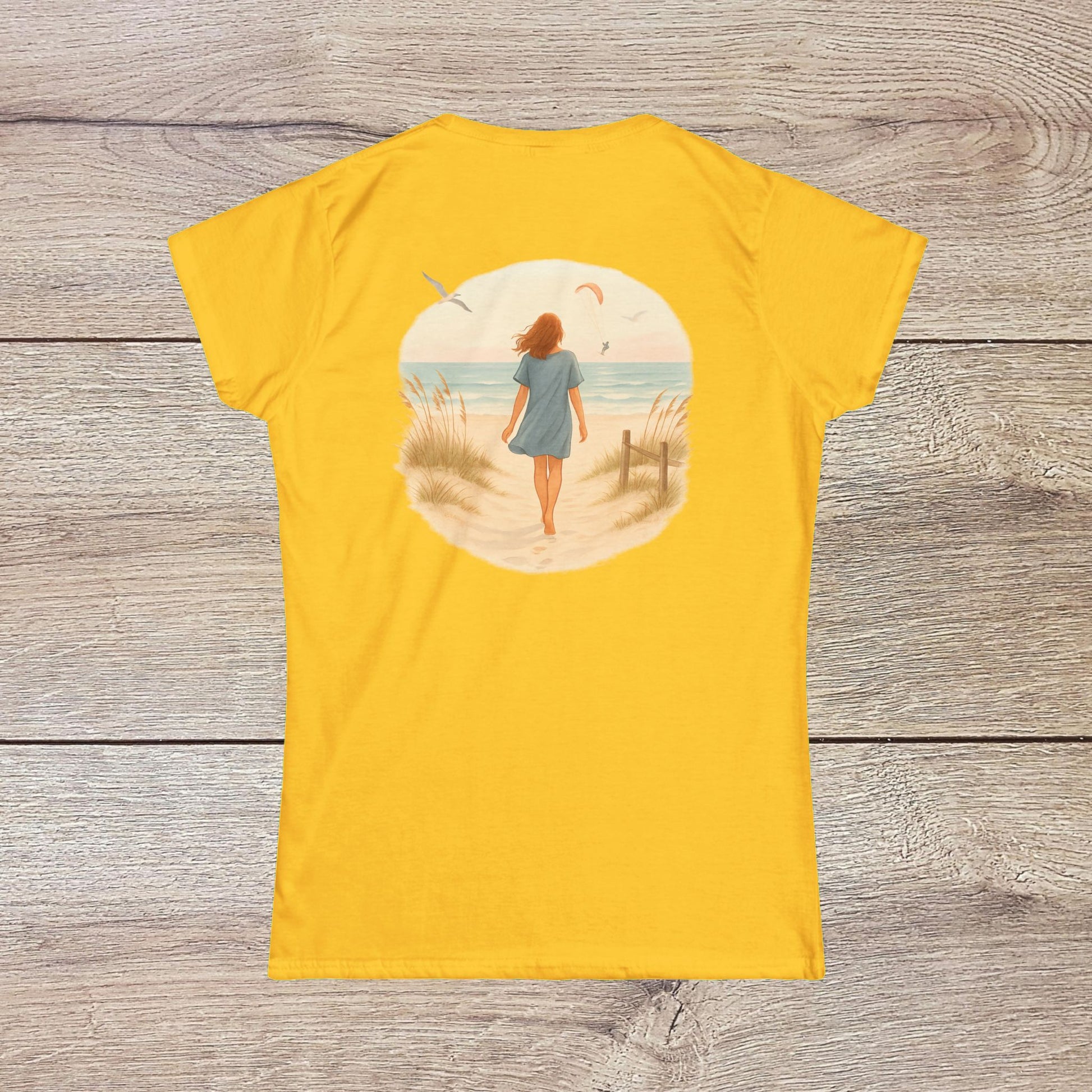 Back view of a woman wearing the vibrant yellow Women's Coastal Spirit Midweight Cotton Tee while strolling on the beach, capturing the essence of coastal lifestyle.