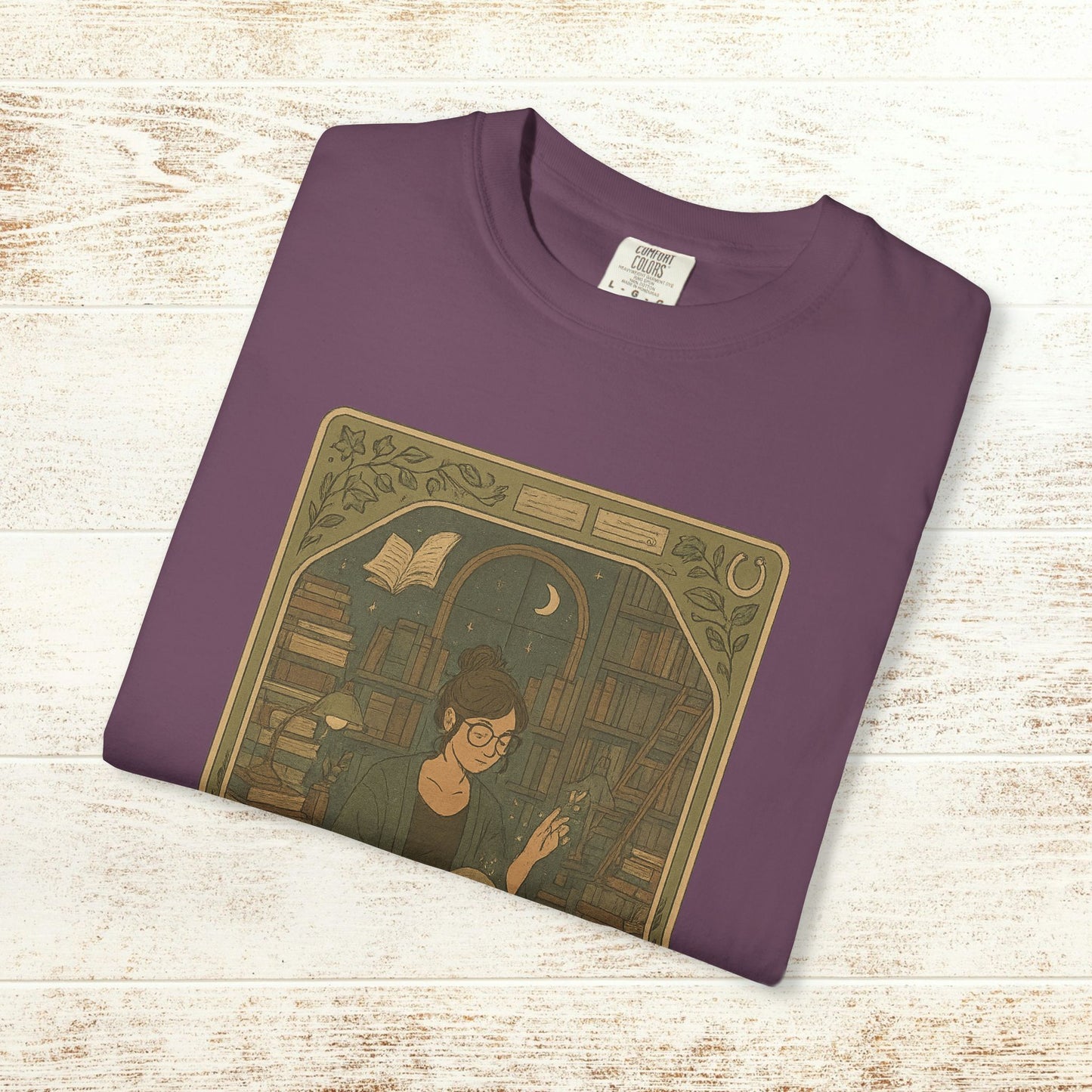 Page Turner Tarot Tee in deep purple, showcasing a creative illustration of a woman among books, made from soft and environmentally friendly cotton fabric.