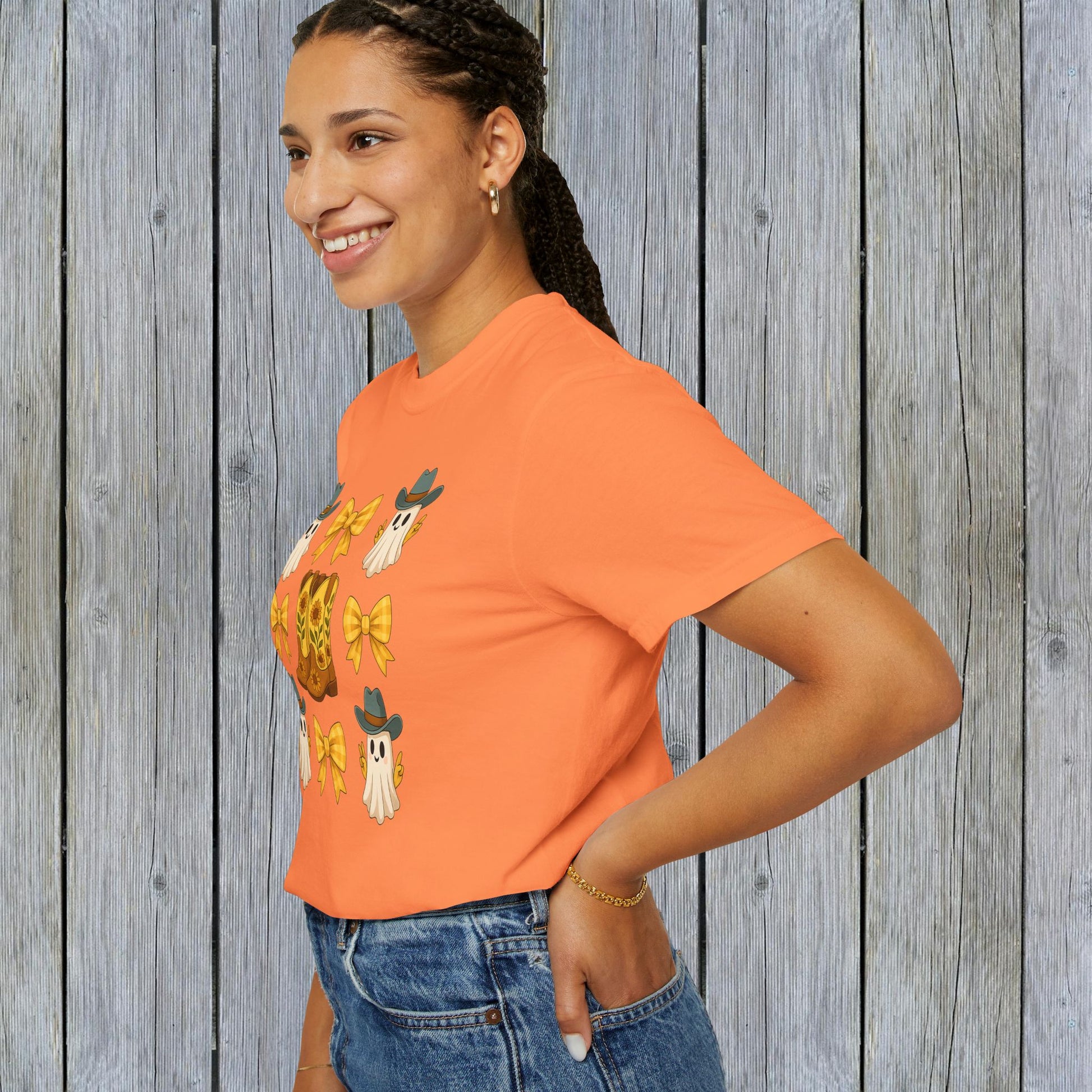 Cute Halloween T-Shirt in bright orange, worn by a woman showcasing ghosts and cowboy boots. Ideal for unisex fall fashion crafted from eco-friendly materials.