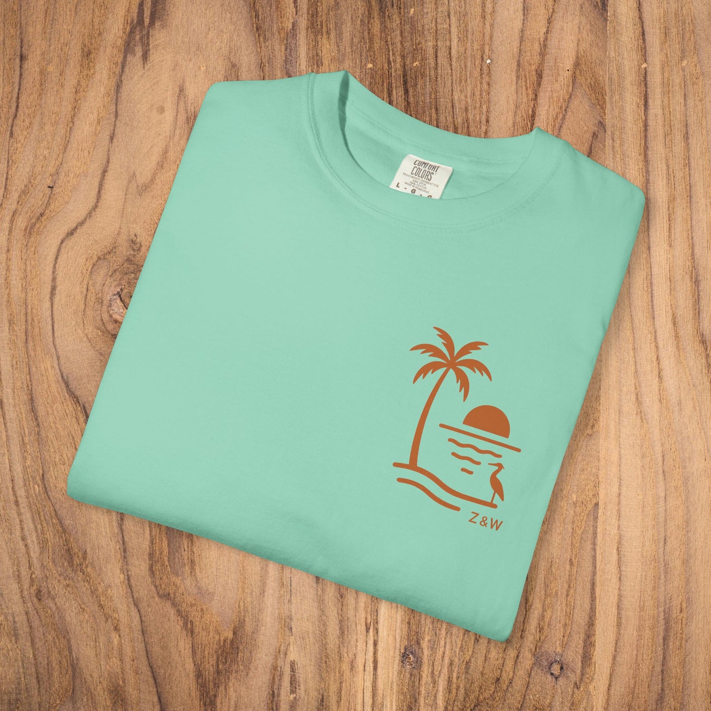 Unisex Sunset Palm Tree T-Shirt shown flat in a refreshing mint green color, adorned with a modern palm tree and sunset print, made from soft garment-dyed cotton for ultimate comfort.