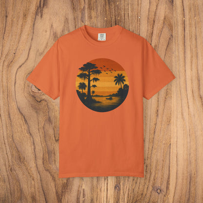 Unisex Garment-Dyed Sunset Tee in bright orange color showcasing a stunning sunset design with palm trees and flying birds. Made of soft 100% cotton, available in sizes S to 4XL.