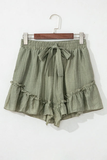 Textured Tie Waist Ruffle Hem Shorts in a soft olive green fabric, showcasing a stylish ruffle hem and a tie waist detail.