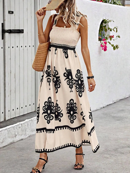 Trendsi Smocked Printed Maxi Dress with Wide Straps - Elegant Opaque, Non-Stretch Design showcasing a model wearing a beige dress with intricate black patterns, accessorized with a straw hat and a woven bag, set against a bright outdoor backdrop.