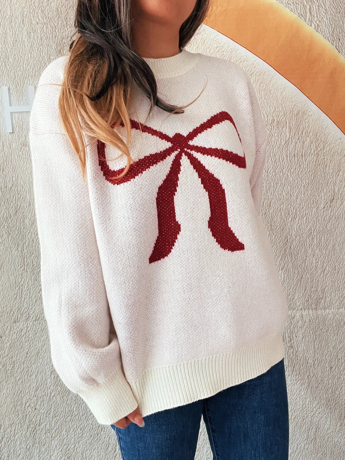Stylish Bow Pattern Casual Long Sleeve Sweater for Effortless Everyday Wear, emphasizing a unique red bow motif on a soft pink sweater, worn with casual jeans.