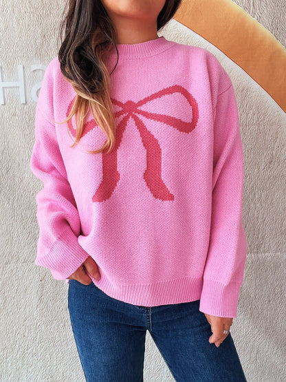 Chic pink long sleeve sweater with a stylish bow pattern, designed for effortless everyday wear. Worn by a model.